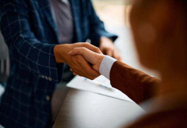 istockphoto-1480535737-612×612 Close up of coworkers handshaking while greeting during business meeting in the office.